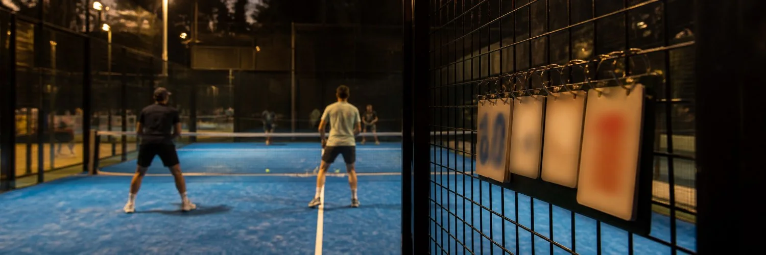 Anzeigetafel an einem Padelcourt mit Spielstand, im Hintergrund zwei Spieler an der Grundlinie