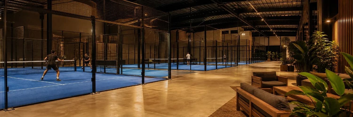 Moderne Indoor-Padelhalle mit mehreren blauen Courts hinter Glaswänden